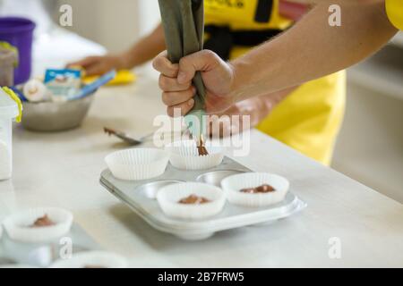 Frau professioneller Konditormeister verteilt Schokoladenteig in Backform. Stockfoto