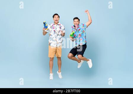 Smilng glückliche asiatische Männerfreunde, die mit Wasserpistolen spielen und in blau isoliert auf den Hintergrund für das Songkran Festival in Thailand und Südostasien springen Stockfoto