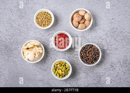 Mix aus aromatischen Gewürzen Koriander, schwarzem Pfeffer, Bergamot, getrocknetem Ingwer, Muskatnuss, Paprika in weißen Körbchen auf grauem Betongrund Top View Flat Lie HE Stockfoto