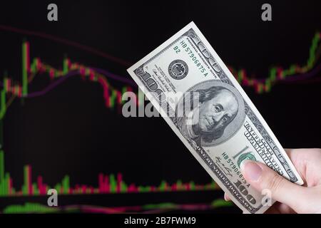 Hände, die Dollar vor einem Laptop-Monitor mit einem Kursdiagramm halten.Forex und trading.A Händler handeln Aktien, Anleihen und Wertpapiere oder Währungen auf t Stockfoto