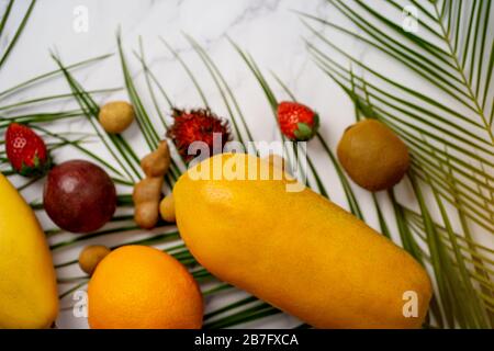 Draufsicht über exotische tropische Früchte und grüne Palmblätter auf weißem Hintergrund. Papaya, Mango, Londan, Tamarind, Erdbeere, Rambutan, Passionsfrucht, KI Stockfoto