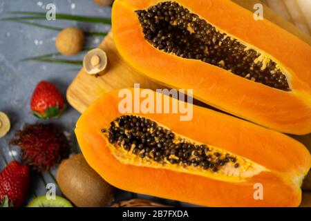 Papaya. Tropische Früchte. Nahaufnahme von zwei Hälften reifer Papaya mit Samen auf Holzschneidebrett. Papaya in Scheiben und andere exotische Früchte auf dem Tisch Stockfoto