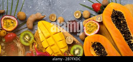 Sommerzusammensetzung von halbpapaya, Drachenfrucht, Rambutan, Tamarind, Mango, Passionsfrucht, Kiwi, Erdbeere, Blättern. Flaches Lay. Draufsicht von t Stockfoto