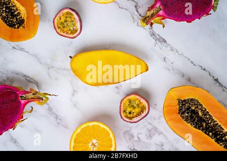 Frische exotische Früchte auf hellem Hintergrund. Hälfte der reifen Papaya, Mango, Passionsfrucht, Orange, Drachenfrucht auf weißem Marmortisch. Draufsicht. Horizontal Stockfoto