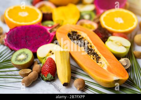 Set aus in Scheiben geschnittenen exotischen frischen Früchten. Verschiedene reife, saftige tropische Sommerfrüchte und tropische Blätter auf weißem Tisch. Selektiver Fokus. Horizontal Stockfoto