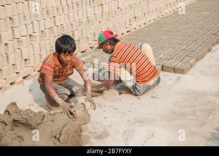 Eine Kinderarbeit in Bangladesch arbeitet in einem Backstein, der unter einem sonnigen Tag abgelegt wird. Obwohl Kinderarbeit in dieser Branche eingeschränkt ist, arbeitet er für Lebensmittel. Stockfoto