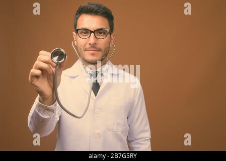 Junger gutaussehender hispanischer Mann Doktor vor braunem Hintergrund Stockfoto