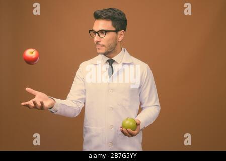 Junger gutaussehender hispanischer Mann Doktor vor braunem Hintergrund Stockfoto