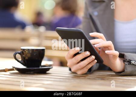 Nahaufnahme der Hände der Frau mit ihrem Handy auf einer Café-Terrasse