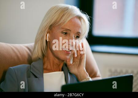 Porträt einer modernen, reifen Geschäftsfrau, die mit Laptop arbeitet und während eines Videoanrufs im Büro mit dem Mikrofon spricht, Kopierraum Stockfoto