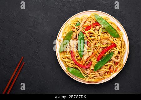Huhn Lo Mein in weißer Platte mit dunklem Schieferhintergrund. Lo Mein ist ein chinesisches Gericht mit Hühnerfleisch, Eiernudeln, Gemüse und Soßen. Kacheln Stockfoto