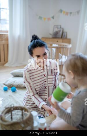 Mutter, die Binde auf das Bein des Kindes anwendet, Mädchen hält Flasche Stockfoto