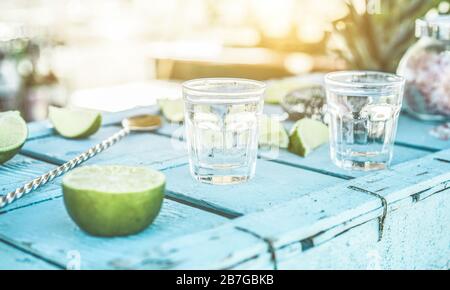 Tequila-Aufnahmen mit Limes und Salz an der blauen Holzbar bei Sonnenuntergang - Latin, Summer, Cocktails, Getränke und Party-Konzept - konzentrieren sich auf linkes Glas Stockfoto