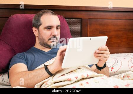 Kranker Mann mit Tablette im Bett. Stockfoto