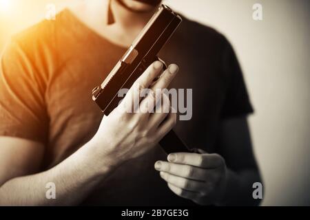 Ein unbekümmter Mann in einem T-Shirt steht mit einer Pistole in den Händen im Gloom und wechselt darin die Zeitschrift. Stockfoto