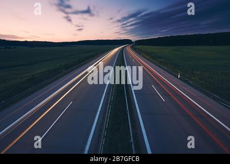 Leichte Wege von Autos. Verkehr auf der Autobahn mitten auf den Feldern bei strahlender Morgendämmerung. Stockfoto