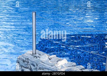 Modernes Schwimmbad mit wunderschönem blauem Wasser, Edelstahltreppe und einem Sicherheitsseil. Stockfoto