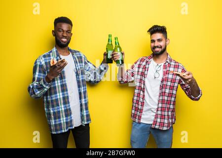 Porträt eines zwei fröhlichen jungen Mannes, der Bier trinkt und Pizza isst, isoliert über gelbem Hintergrund Stockfoto