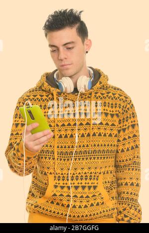 Studio shot der Jungen mit Handy beim Tragen der Kopfhörer um den Hals Mann Stockfoto