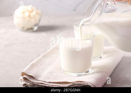 Kefir oder Ayran Gärgetränk wird in ein Glas aus einer Kanne gegossen, ebenso wie Hüttenkäse in einer Schüssel auf hellgrauem Grund, Copy Space Stockfoto