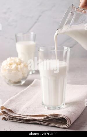 Kefir oder Ayran Gärgetränk wird aus einer Kanne in ein Glas gegossen, ebenso wie Hüttenkäse in einer Schüssel auf hellgrauem Grund, nah beieinander Stockfoto