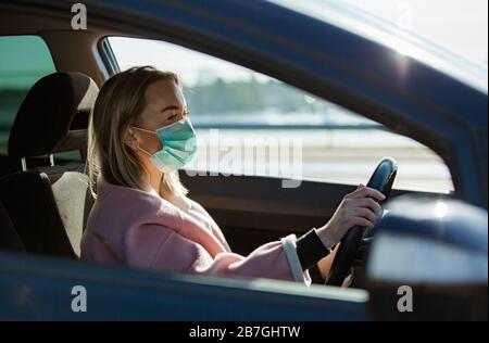 Frau in Schutzmaske, die ein Auto auf der Straße fährt. Sicheres Reisen. Stockfoto