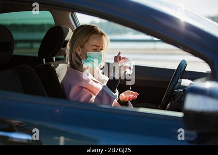 Frau in Schutzmaske mit Händededesinfektionsmittel in einem Auto auf der Straße sitzend. Sicheres Reisen. Stockfoto