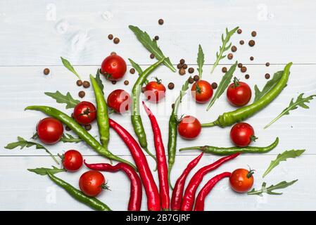 Kirschtomaten in der Nähe von Paprika als Dekoration. Tomaten halbiert mit heißem, würzigen Pfeffer auf grauem Holzhintergrund. Vegetarisches Kunstkonzept. Lebensmittel für die Dekoration mit Gewürzen und Gemüse Stockfoto
