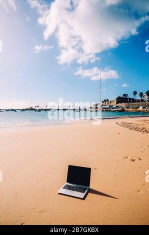 Generisches Notebook Laptop am sonnigen, einsamen sandigen Strand im Hintergrund. Paradise Home Office Konzept speziell bei Coronavirus Covid-19 Ausbruch Stockfoto