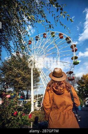 Frau mit Hut und Kamera in der Nähe Riesenrad im Herbst Park betrachten Stockfoto