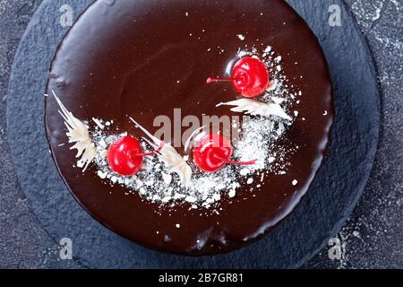 Süßschokolade und Maraschinokirschen mit Kirschkuchen, gefüllt mit dunkler Schokoladenglasur, die mit weißer Schokolade und Konserven verziert ist Stockfoto