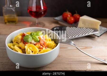 Hausgemachtes Dinner Tortellini mit Tomatensauce arrabbiata und Käse mit einem Glas Wein auf der Seite. Stockfoto