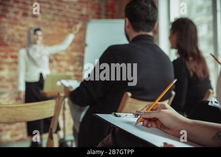 Weibliche muslimische Referentin, die in der Halle auf dem Workshop vorstellend ist. Publikum oder Konferenzsaal. Nahaufnahme des schreibenden Teilnehmers. Konferenzveranstaltung, Schulung. Bildung, Vielfalt, integratives Konzept. Stockfoto