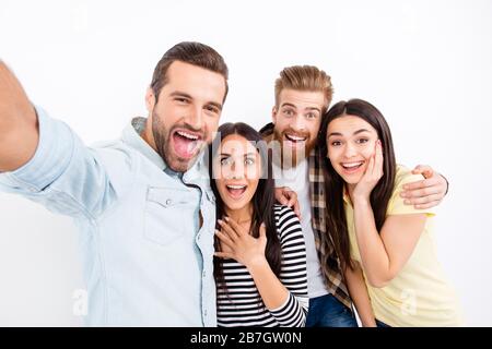 Gruppe von aufgeregten Freunden, die selfie auf der Kamera des Smartphones machen und dabei auf weißem Hintergrund in ungezwungener Atmosphäre große Emotionen von Verwunderung und Aufregung zeigen Stockfoto