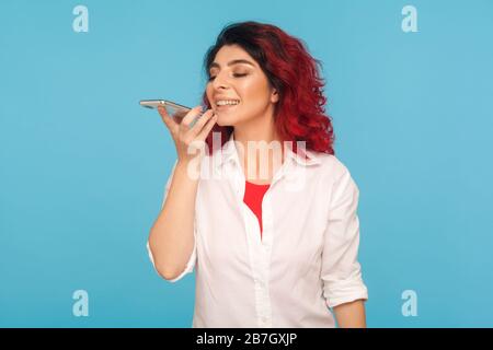 Innovative Technologien. Hipper Frau mit fantasievolle roten Haaren, die den Sprachassistenten am Handy fragt, die Aufgabe gibt und mit künstlicher Intelligenz im Mo spricht Stockfoto