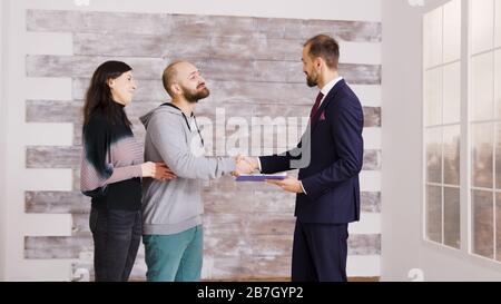 Immobilienmakler in Geschäftsanzug, der jungen Paaren nach Unterzeichnung des Dokuments Schlüssel gibt. Paar wird Hausbesitzer. Stockfoto