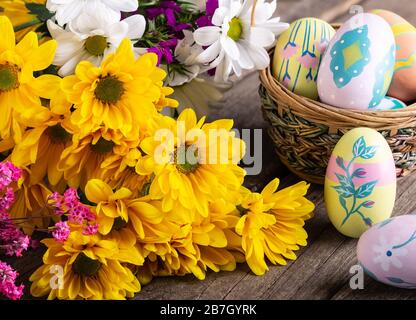 Blumenstrauß aus wunderschönen gelben Gänseblümchen und bunten ostereiern auf einer Holzoberfläche Stockfoto