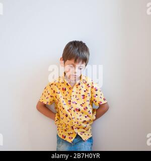 Betonen Sie das Konzept des "Stressmind State" für aufgebrachten kleinen Jungen im Hemd, das sich an die Wand lehnt Stockfoto