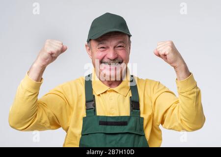 Leitender Arbeiter, Mann in grüner Mütze und Kleidung, die aufgeregt die Fäuste hochhalten. Stockfoto