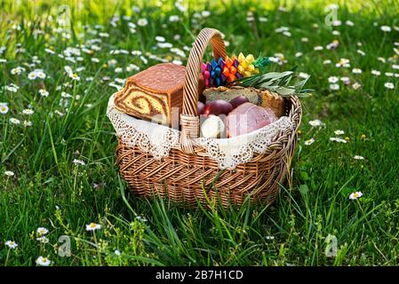 Ostern traditionelle Küche mit Schinken, Eiern und Brot im Korb. Urlaub im Freien. Osterkorb mit allerlei köstlichen Delikatessen gefüllt Stockfoto