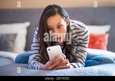 Frau, die in ihrem Zuhause auf dem Bett liegt und Smartphone verwendet. Stockfoto