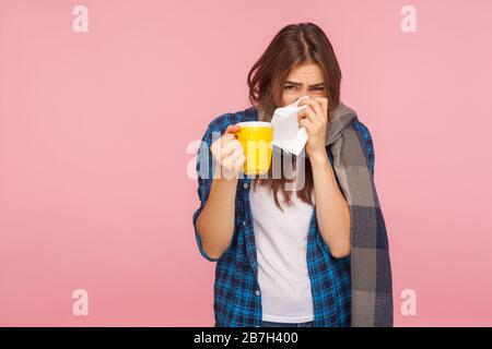 Behandlung der saisonalen Grippe. Krankes Mädchen, das in Schal gehüllt ist, die laufende Nase weht, in Serviette niest und Teetasse hält, Influenza, Husten und Fieber behandelt. Stockfoto