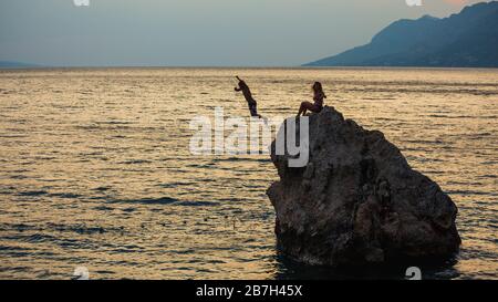 Junge Leute springen aus großem Stein, Brela, Kroatien, ins Wasser. Stockfoto