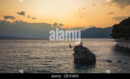 Junge Leute springen aus großem Stein, Brela, Kroatien, ins Wasser. Stockfoto