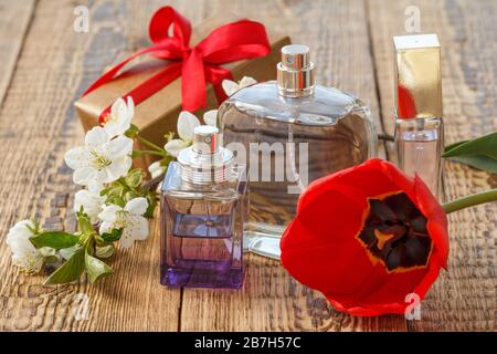 Geschenkschachtel mit rotem Band und Parfümflaschen auf Holzbrettern mit roten Tulpen- und Jasminblüten auf alten Holzbrettern. Stockfoto