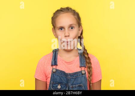 Portrait des komischen kleinen Mädchens in Denim-Overalls, das Fisch mit Pout-Lippen ins Gesicht stellt, Kind, das mit humorvoller dummer Ausdrucksweise auf die Kamera blickt. indo Stockfoto