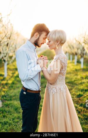 Glückliches schönes kaukasisches Paar, Hände halten und die Stirn berühren, verbringen Sie Zeit im Frühling blühenden Baumgarten. Frohe Frühling oder ostern Stockfoto