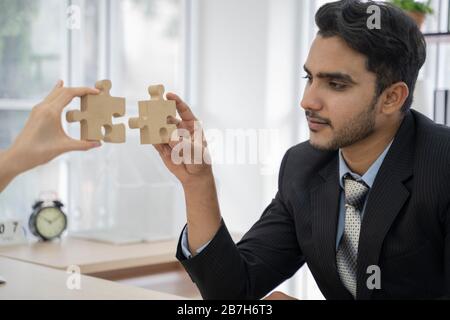 Ein asiatisches Geschäftsleute sitzt am Büroschreibtisch, stellt Puzzleteile zusammen und findet Lösung. Stockfoto