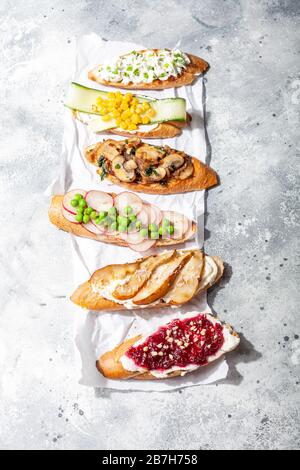 Verschiedene Bruschetta- oder Tapas-Sets mit verschiedenen Belägen auf Betongrund. Italienische Vorspeise, offenes Toast-Sandwich mit Pilzen, Erbsen, Gurken, Mais und pe Stockfoto