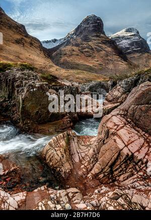 Der Fluss Coe, der im Winter durch Glen Coe fließt, mit der Gruppe der Berge, die im Hintergrund als The Three Sisters bekannt ist Stockfoto